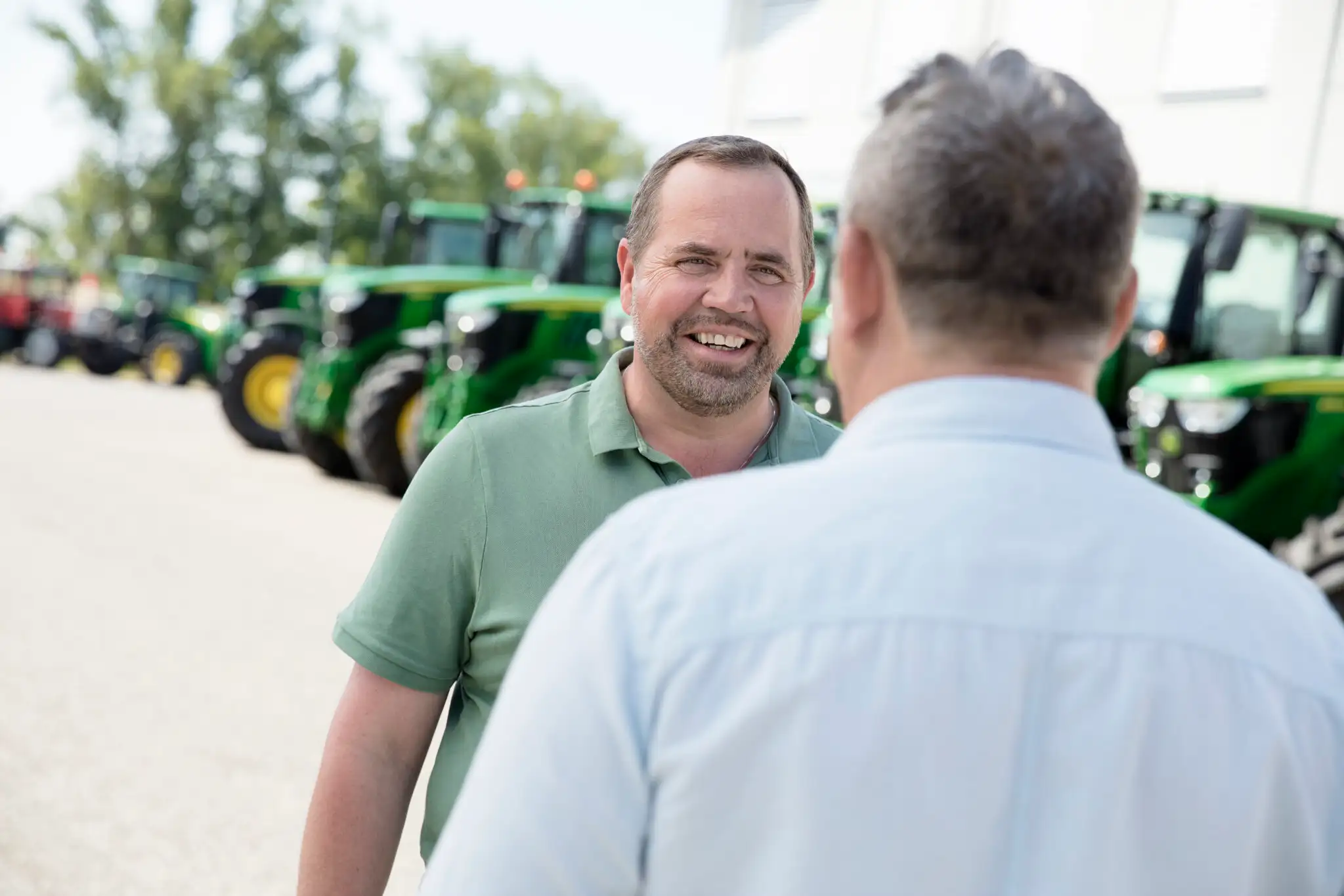 Zwei Männer in einem Verkaufsgespräch. Im Hintergrund sieht man viele John Deere Traktoren