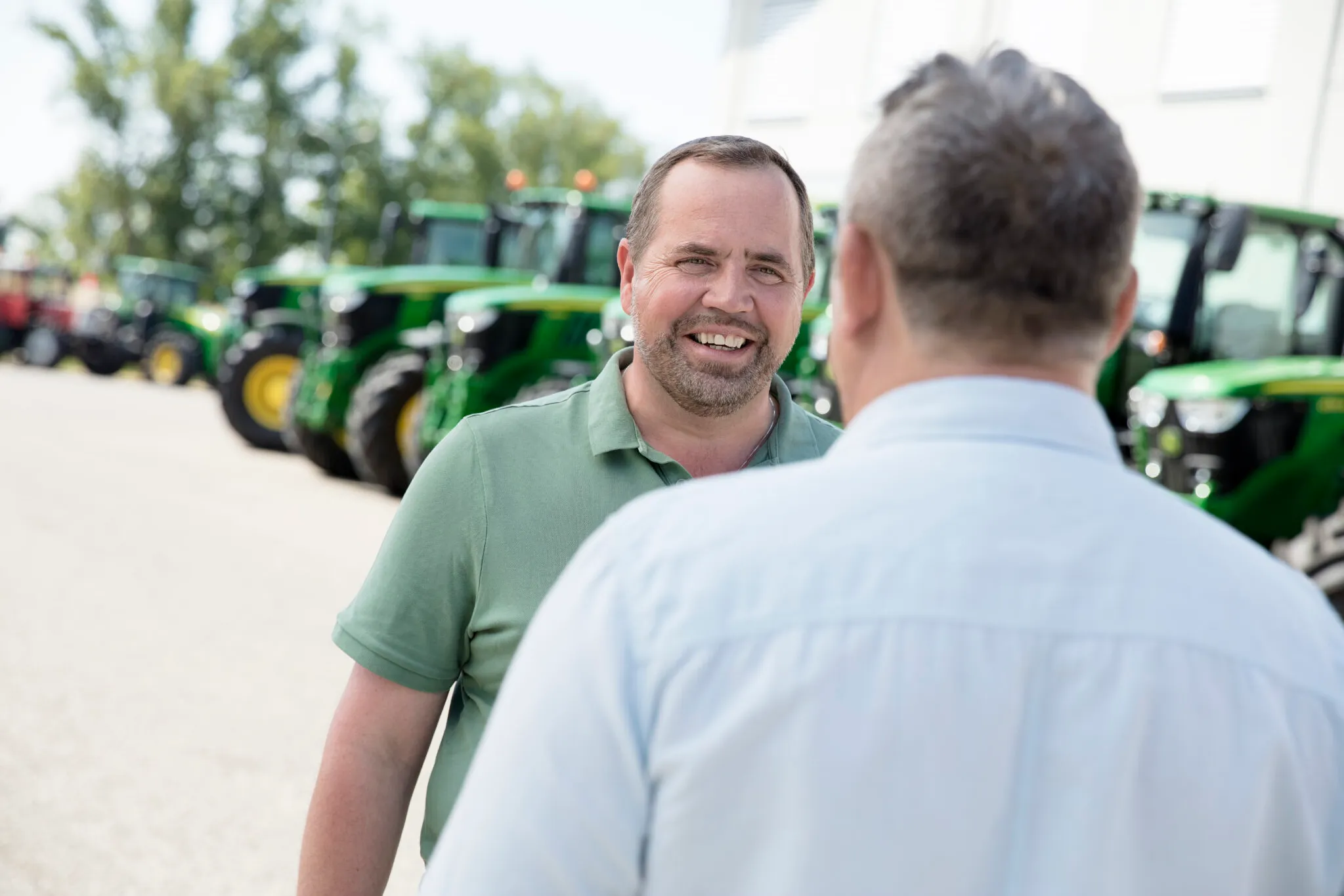 Zwei Männer in einem Verkaufsgespräch. Im Hintergrund sieht man viele John Deere Traktoren